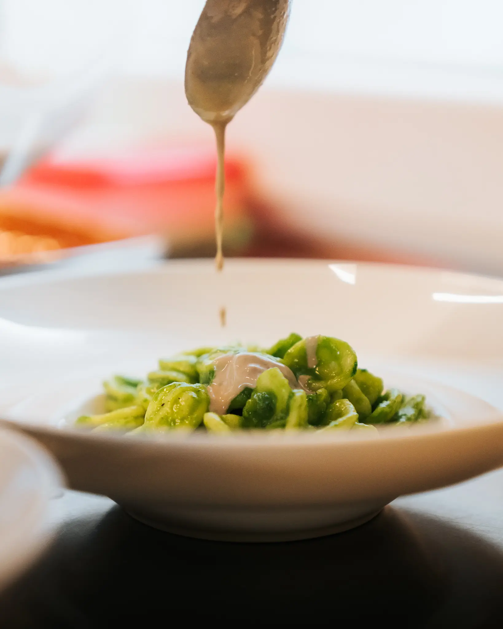 Cucchiaio che versa salsa su piatto di pasta fresca – ENOè Vicenza